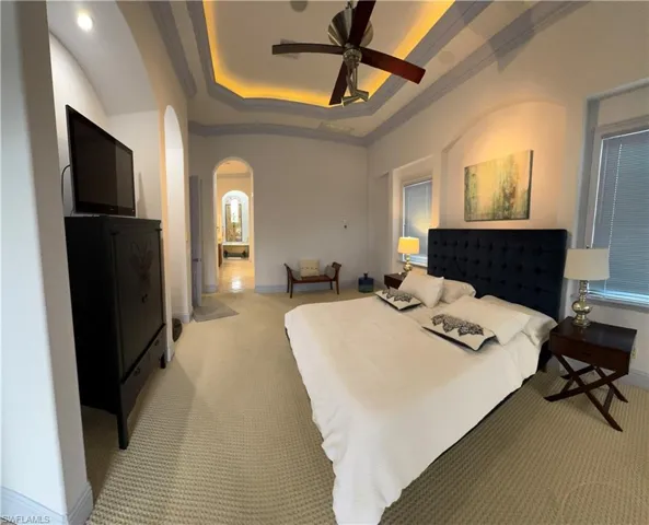 Bedroom with arched walkways, a raised ceiling, ceiling fan, crown molding, and carpet floors