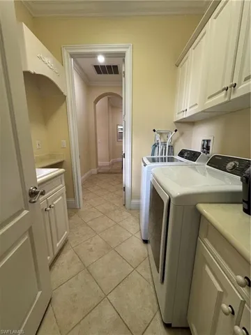 Laundry area with cabinet space, visible vents, arched walkways, washer and clothes dryer, and ornamental molding