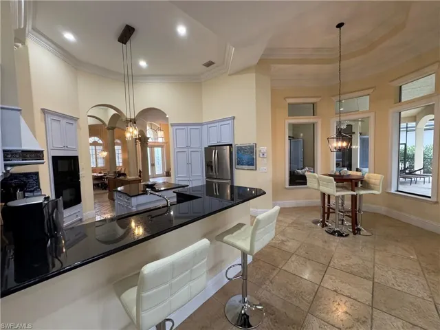 Kitchen with arched walkways, dark countertops, a breakfast bar area, decorative light fixtures, and stainless steel refrigerator with ice dispenser