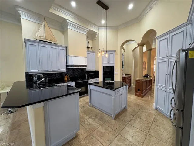Kitchen with arched walkways, hanging light fixtures, freestanding refrigerator, a center island, and dark countertops