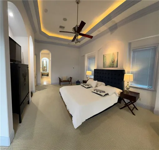 Carpeted bedroom with arched walkways, a raised ceiling, visible vents, ornamental molding, and baseboards