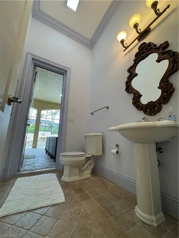 Half bath with stone finish floor, toilet, crown molding, and baseboards