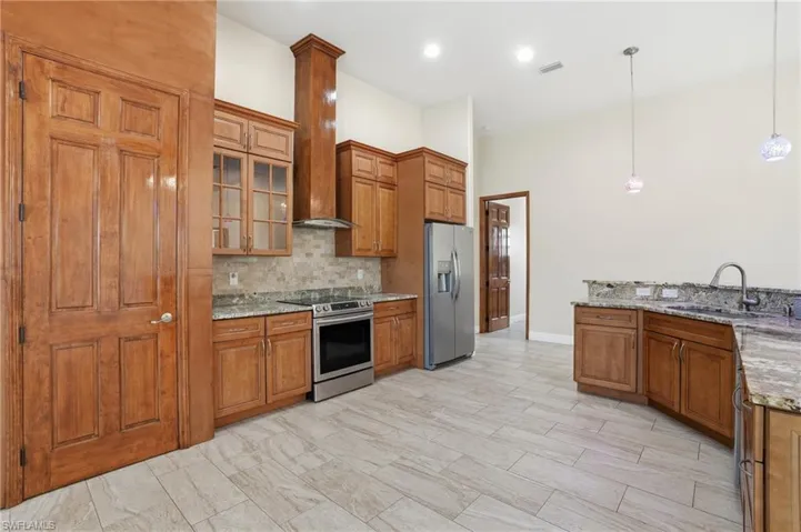 Kitchen featuring brown cabinetry, appliances with stainless steel finishes, hanging light fixtures, light stone counters, and recessed lighting