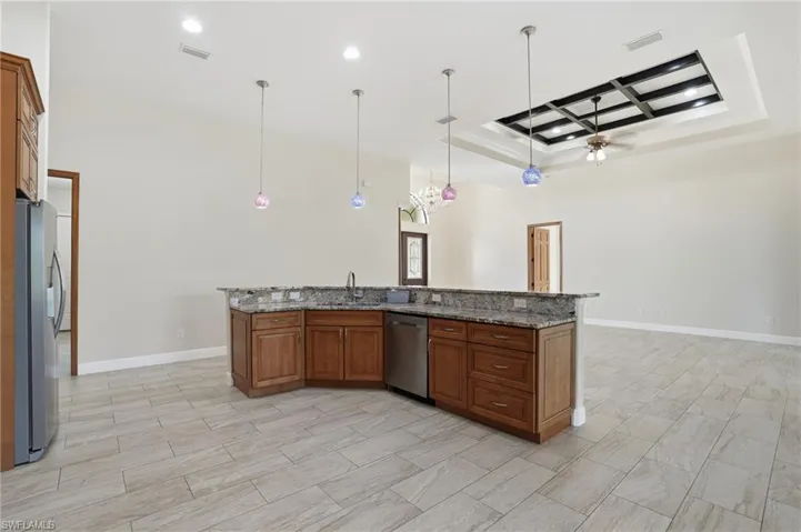 Kitchen with brown cabinetry, hanging light fixtures, dark stone counters, a ceiling fan, and coffered ceiling