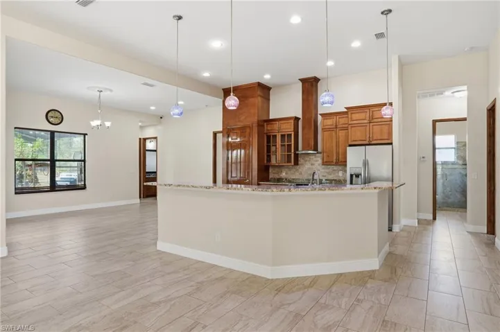 Kitchen with healthy amount of natural light, brown cabinets, decorative light fixtures, light stone counters, and recessed lighting