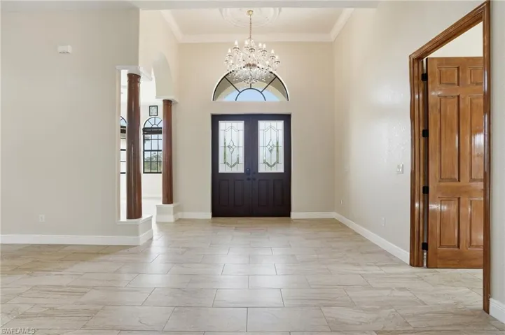 Foyer entrance featuring crown molding, arched walkways, decorative columns, a towering ceiling, and a chandelier