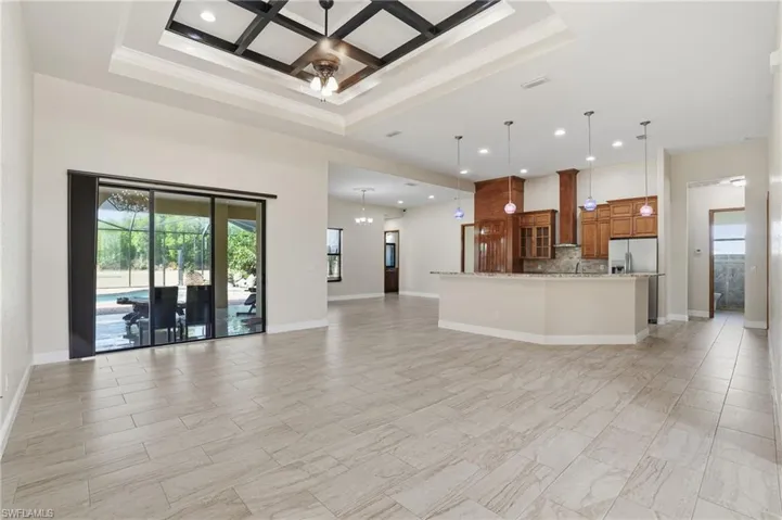 Unfurnished living room with plenty of natural light, a high ceiling, coffered ceiling, recessed lighting, and a chandelier
