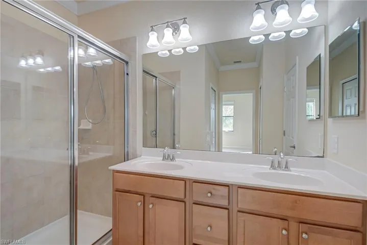 Full bath with ornamental molding, a shower stall, and double vanity
