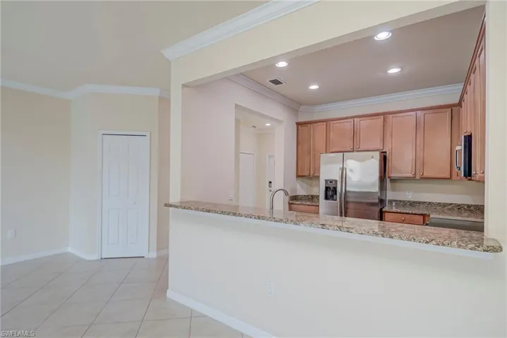 Kitchen featuring stainless steel appliances, light stone countertops, ornamental molding, a peninsula, and light tile patterned floors