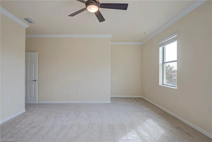 Empty room with ornamental molding, light colored carpet, and a ceiling fan