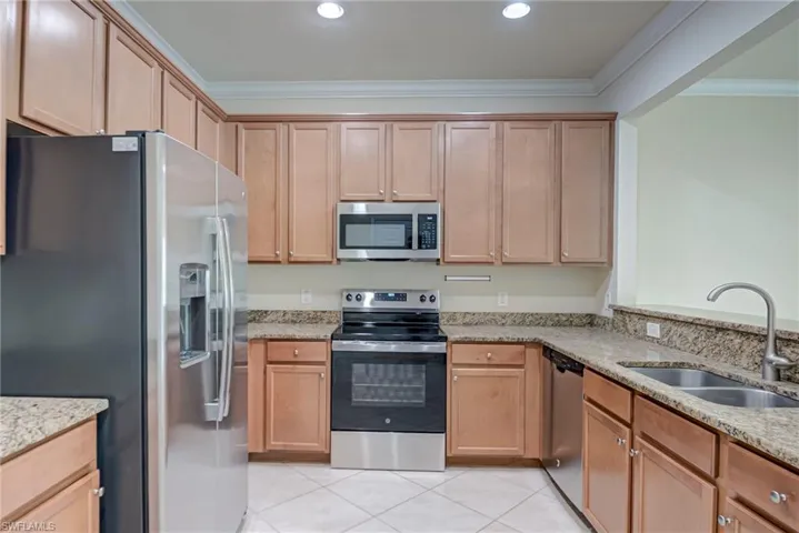 Kitchen with stainless steel appliances, light stone counters, crown molding, and light tile patterned floors