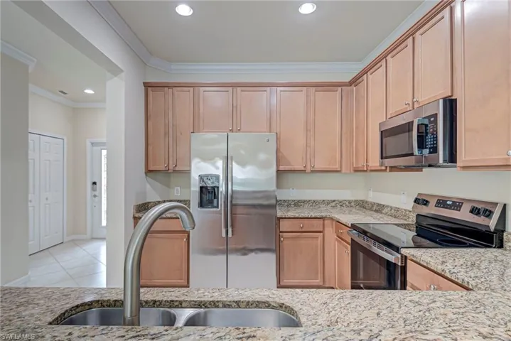 Kitchen with stainless steel appliances, light stone countertops, ornamental molding, recessed lighting, and light tile patterned flooring