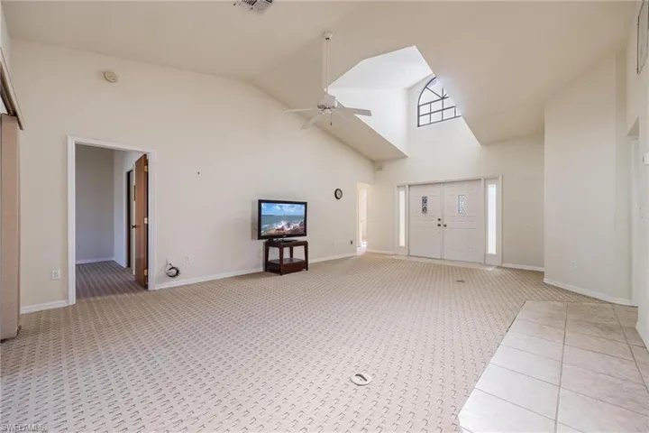 Unfurnished living room with ceiling fan, light carpet, and high vaulted ceiling
