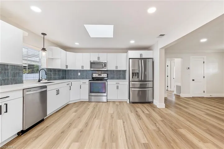 Kitchen with appliances with stainless steel finishes, white cabinets, backsplash, a skylight, and decorative light fixtures