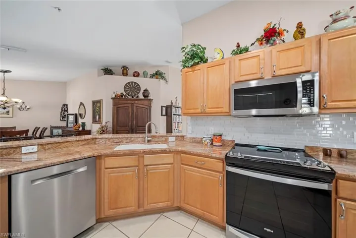 Kitchen with backsplash, sink, light stone countertops, appliances with stainless steel finishes, and light tile patterned flooring