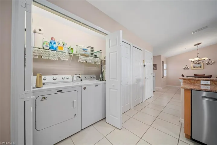 Washroom featuring washer and clothes dryer, light tile patterned floors, and an inviting chandelier