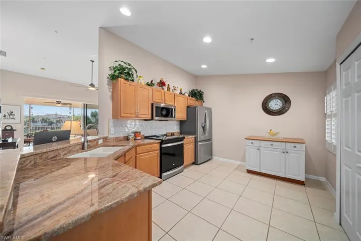 Kitchen with sink, decorative backsplash, light tile patterned flooring, light stone counters, and stainless steel appliances