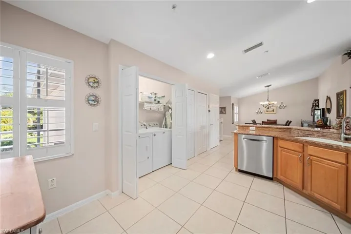 Kitchen with pendant lighting, sink, vaulted ceiling, stainless steel dishwasher, and independent washer and dryer