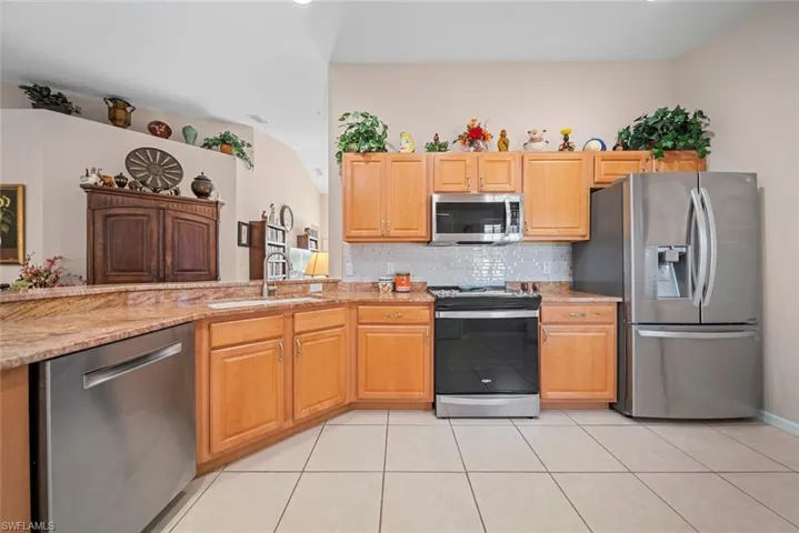 Kitchen featuring decorative backsplash, light stone counters, stainless steel appliances, sink, and light tile patterned floors