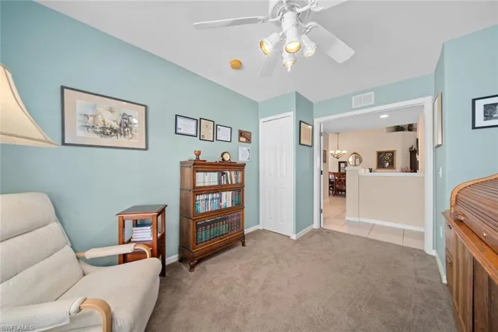 Sitting room featuring light colored carpet and ceiling fan with notable chandelier