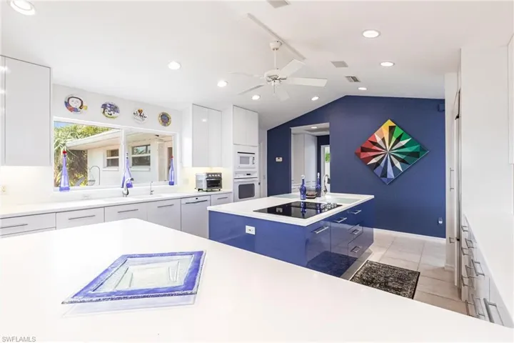 Kitchen featuring white appliances, modern cabinets, white cabinets, vaulted ceiling, and recessed lighting