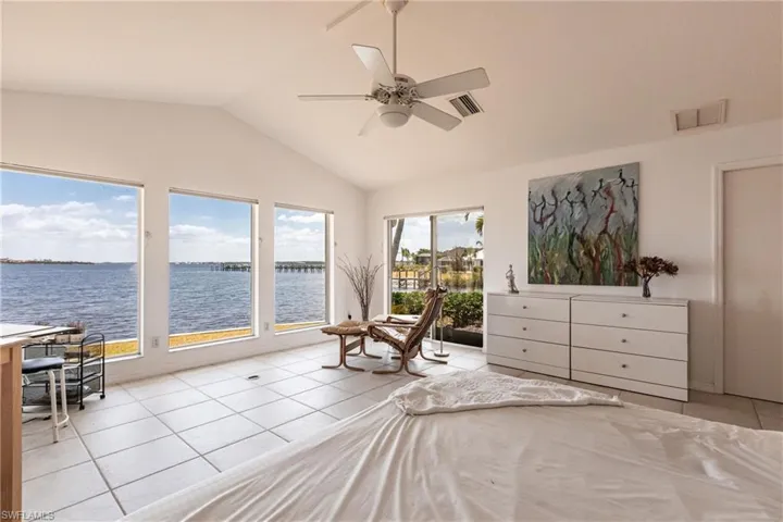 Bedroom featuring light tile patterned flooring, lofted ceiling, a water view, access to exterior, and ceiling fan