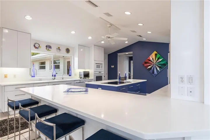 Kitchen featuring white appliances, modern cabinets, a kitchen bar, white cabinetry, and lofted ceiling