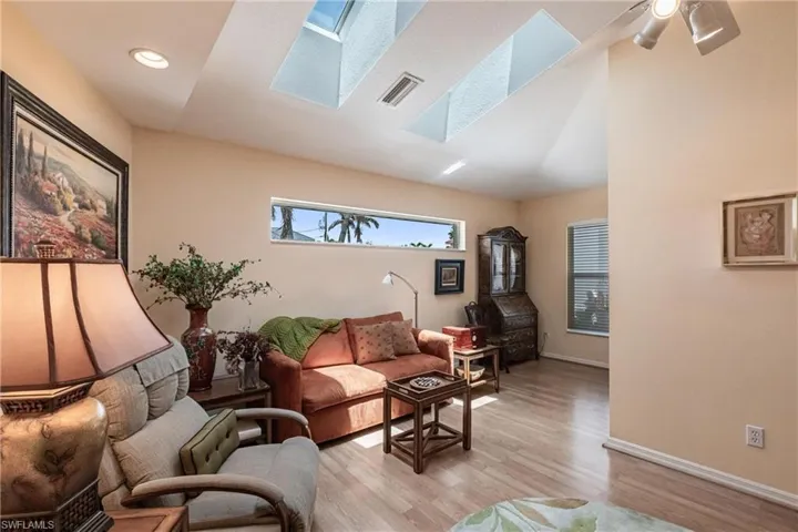 Living area featuring a skylight, light wood-type flooring, baseboards, vaulted ceiling, and recessed lighting