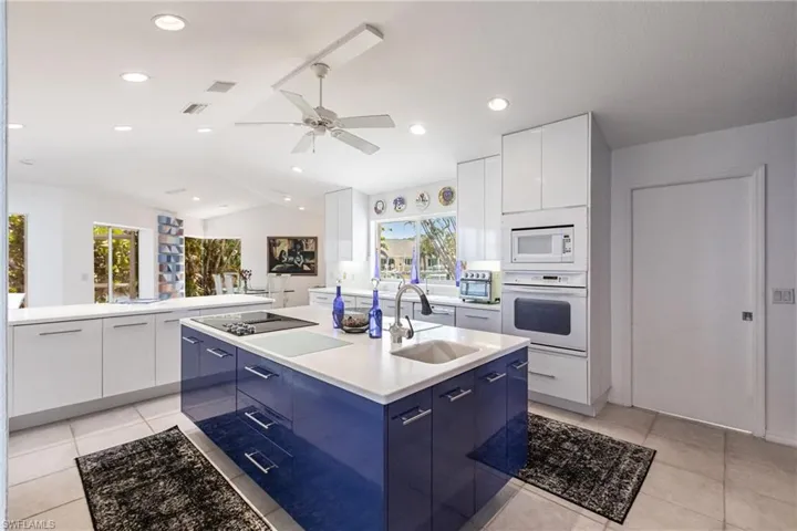 Kitchen with a sink, modern cabinets, white appliances, blue cabinetry, and ceiling fan