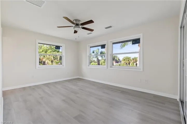 Primary bedroom featuring light wood finished floors, multiple windows, ceiling fan, and a closet
