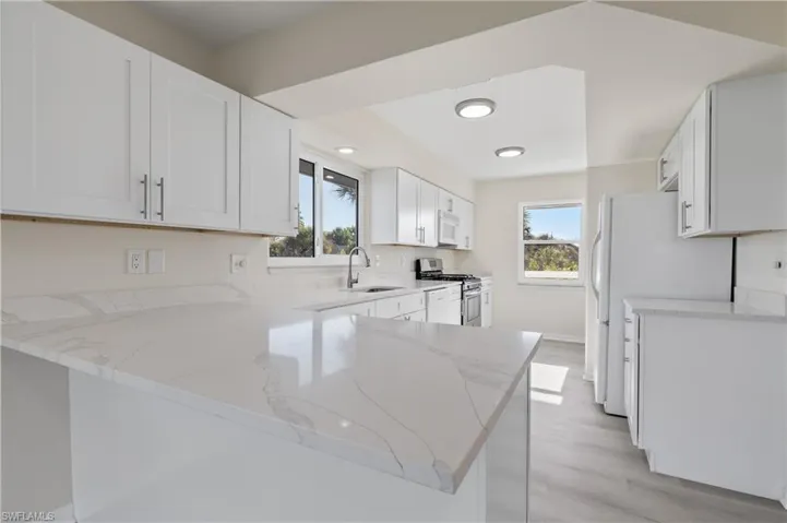 Kitchen featuring a peninsula, white shaker cabinets, light stone countertops, and light LVP wood finished floors