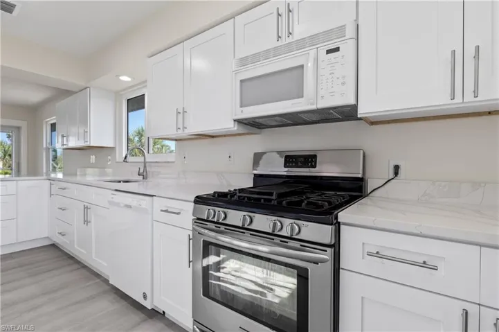 Kitchen featuring white appliances, white cabinetry, light stone counters, and recessed lighting