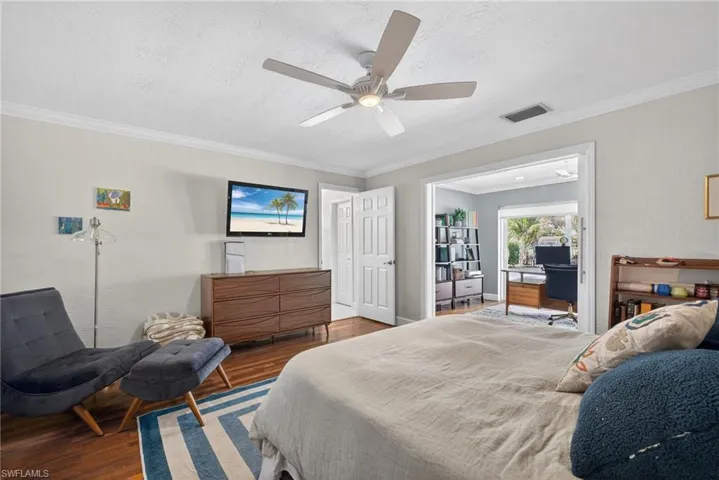Bedroom with wood finished floors, ornamental molding, ceiling fan, a textured wall, and a textured ceiling