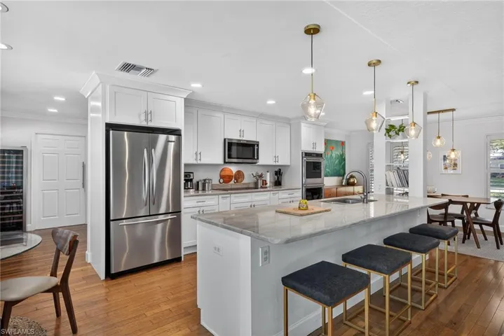 Kitchen with ornamental molding, a breakfast bar area, stainless steel appliances, light stone countertops, and white cabinetry