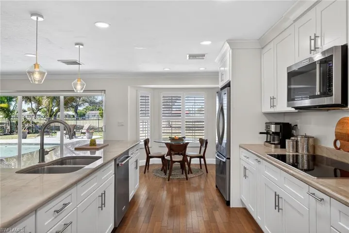 Kitchen with white cabinets, hanging light fixtures, stainless steel appliances, dark wood-type flooring, and plenty of natural light