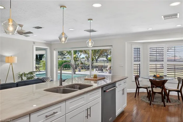 Kitchen with pendant lighting, white cabinetry, light stone countertops, dark wood-style flooring, and stainless steel dishwasher