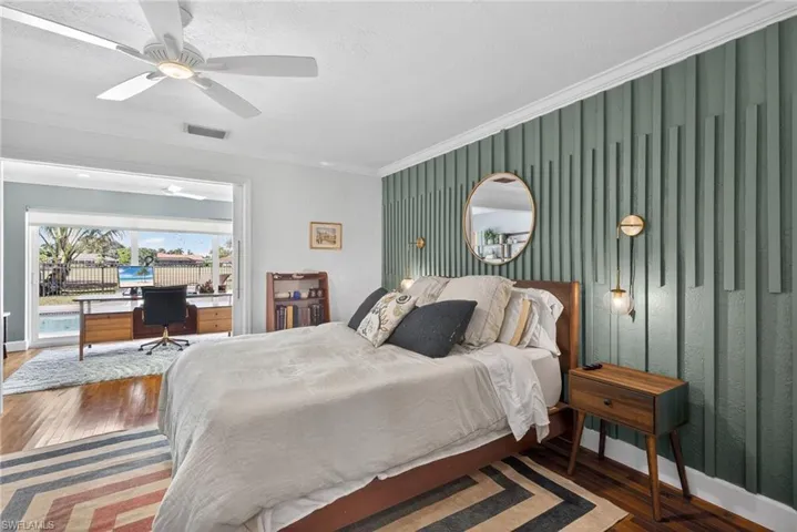 Bedroom with a desk, wood finished floors, ceiling fan, crown molding, and an accent wall