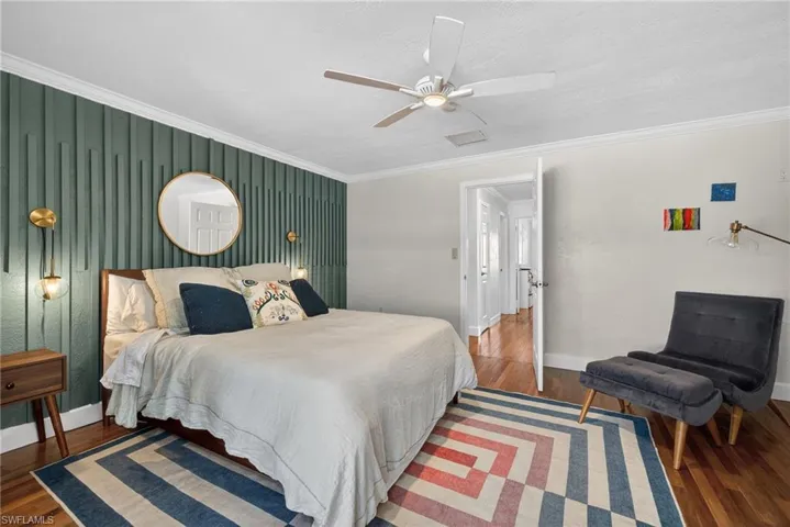 Bedroom with crown molding, wood finished floors, a ceiling fan, and an accent wall