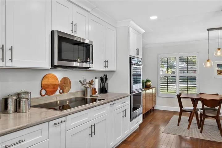 Kitchen with white cabinets, stainless steel appliances, crown molding, dark wood-style flooring, and decorative light fixtures