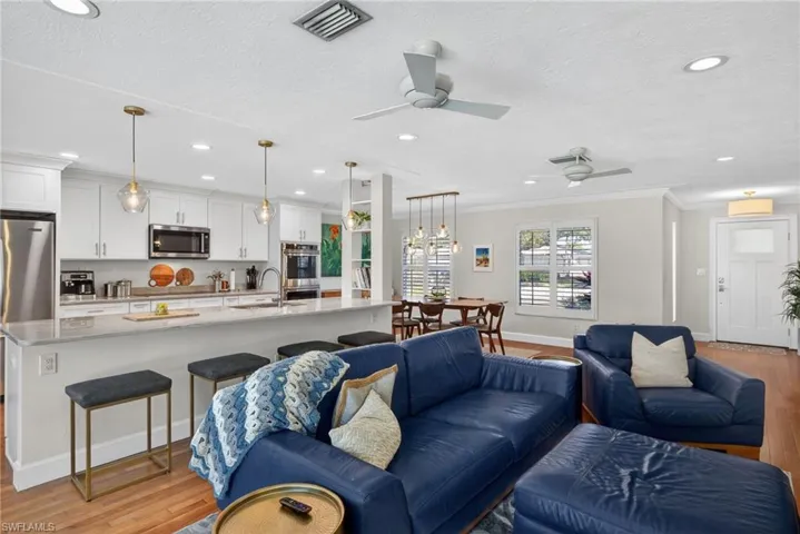 Living room featuring light wood-style flooring, crown molding, a ceiling fan, a textured ceiling, and a chandelier