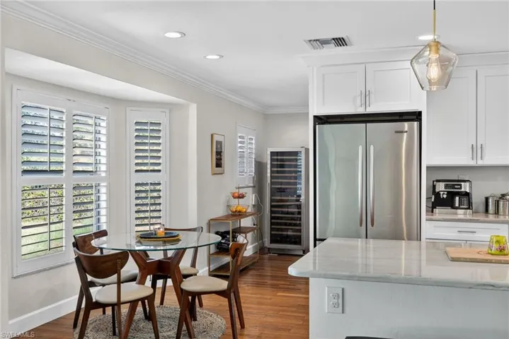 Kitchen featuring white cabinetry, light stone countertops, freestanding refrigerator, wine cooler, and crown molding