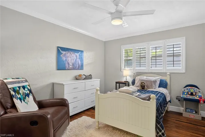 Bedroom with dark wood finished floors, crown molding, a textured wall, and a ceiling fan