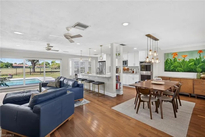 Living area featuring dark wood-style flooring, a ceiling fan, hanging lights, a textured ceiling, and ornamental molding