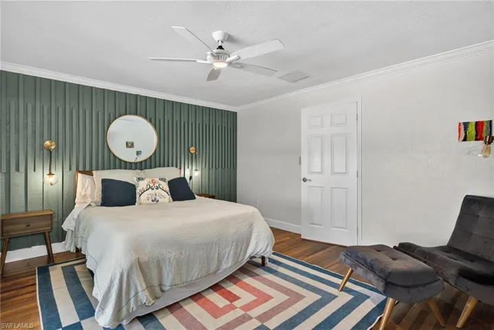 Bedroom with crown molding, a ceiling fan, wood finished floors, an accent wall, and a textured ceiling