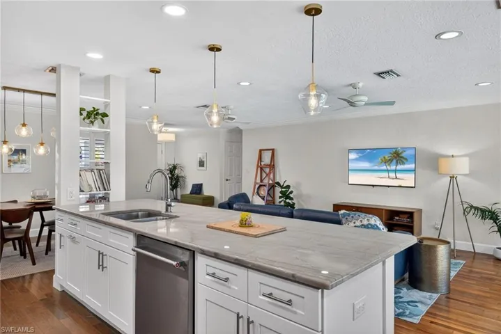 Kitchen featuring open floor plan, decorative light fixtures, stainless steel dishwasher, white cabinetry, and a center island with sink