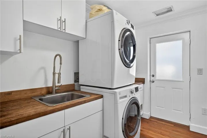 Laundry area with cabinet space, stacked washer and dryer, wood finished floors, and crown molding