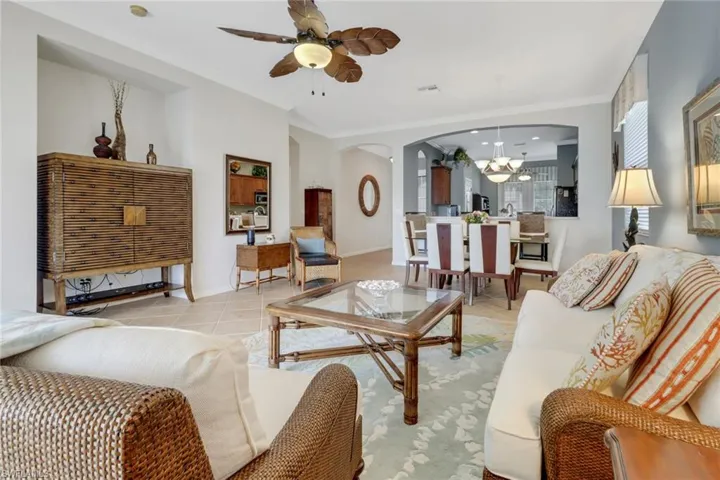 Living area with arched walkways, light tile patterned floors, a chandelier, ornamental molding, and a ceiling fan