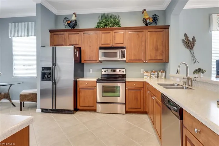 Kitchen with brown cabinetry, appliances with stainless steel finishes, crown molding, light stone countertops, and light tile patterned flooring