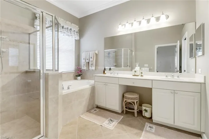 Bathroom with a garden tub, double vanity, a shower stall, light tile patterned floors, and crown molding