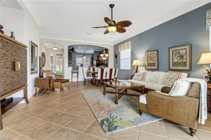 Living area featuring light tile patterned floors, a ceiling fan, arched walkways, and crown molding